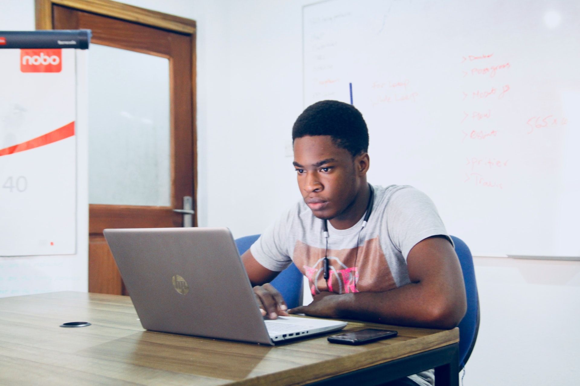 mars-7d4lredspyq-unsplash A young man sits alone in a classroom, looking at his laptop.